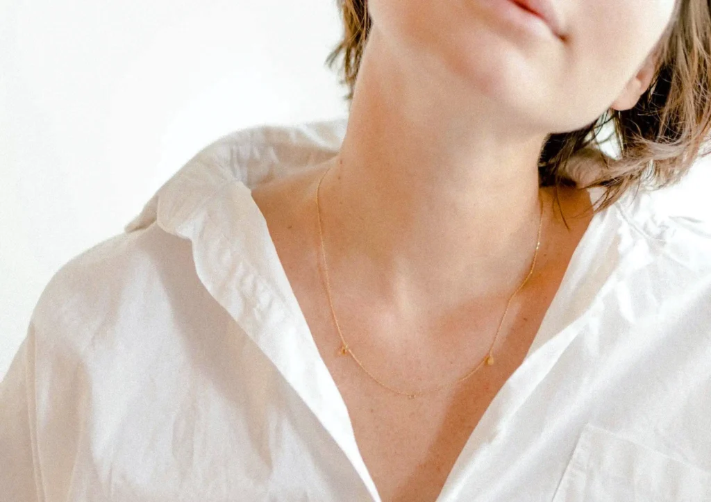 Woman wearing white shirt and necklace showing her neck where thyroid is located