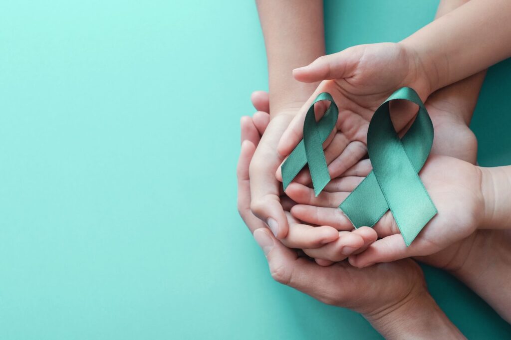Hands holding teal ribbons representing ovarian cancer awareness