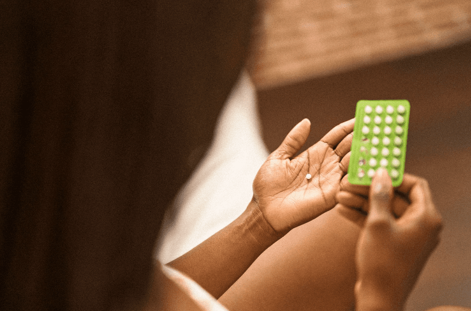 Woman holding birth control pills sitting on a bed